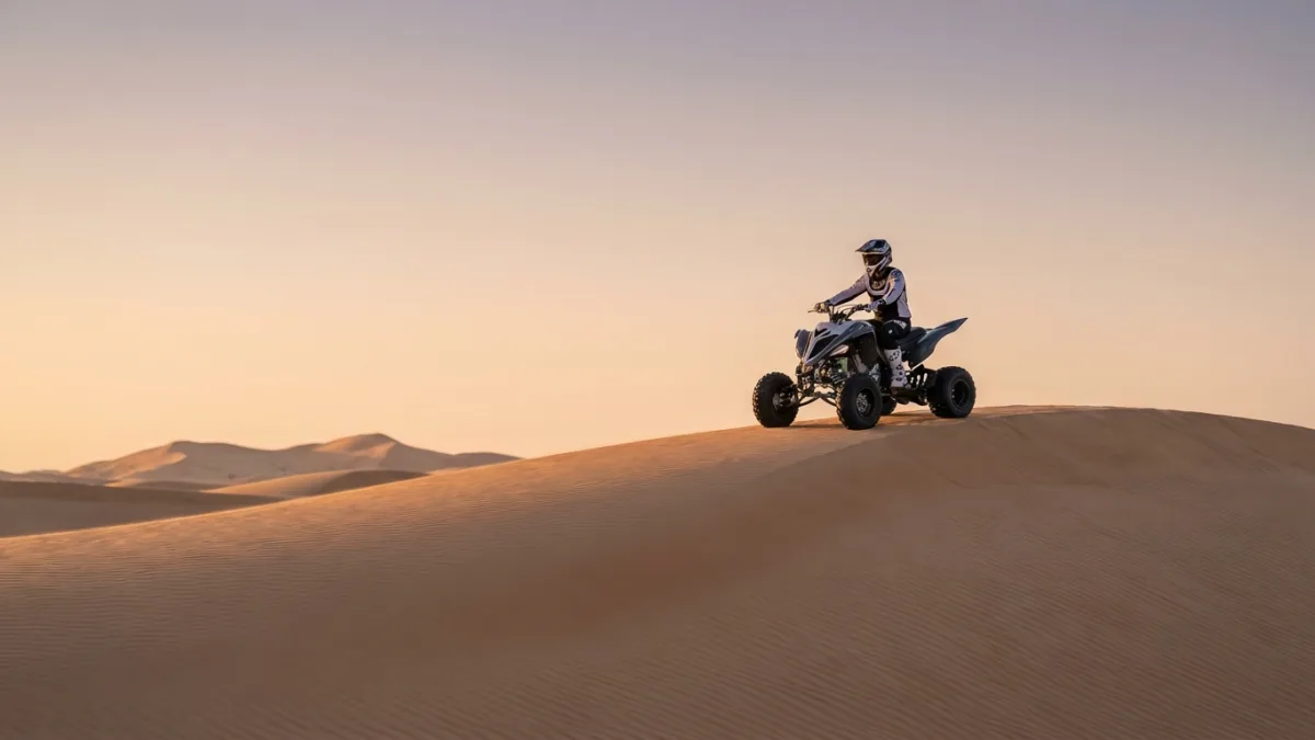 A person riding a quad bike across the towering golden sand dunes of the Abu Dhabi desert under a clear sky.